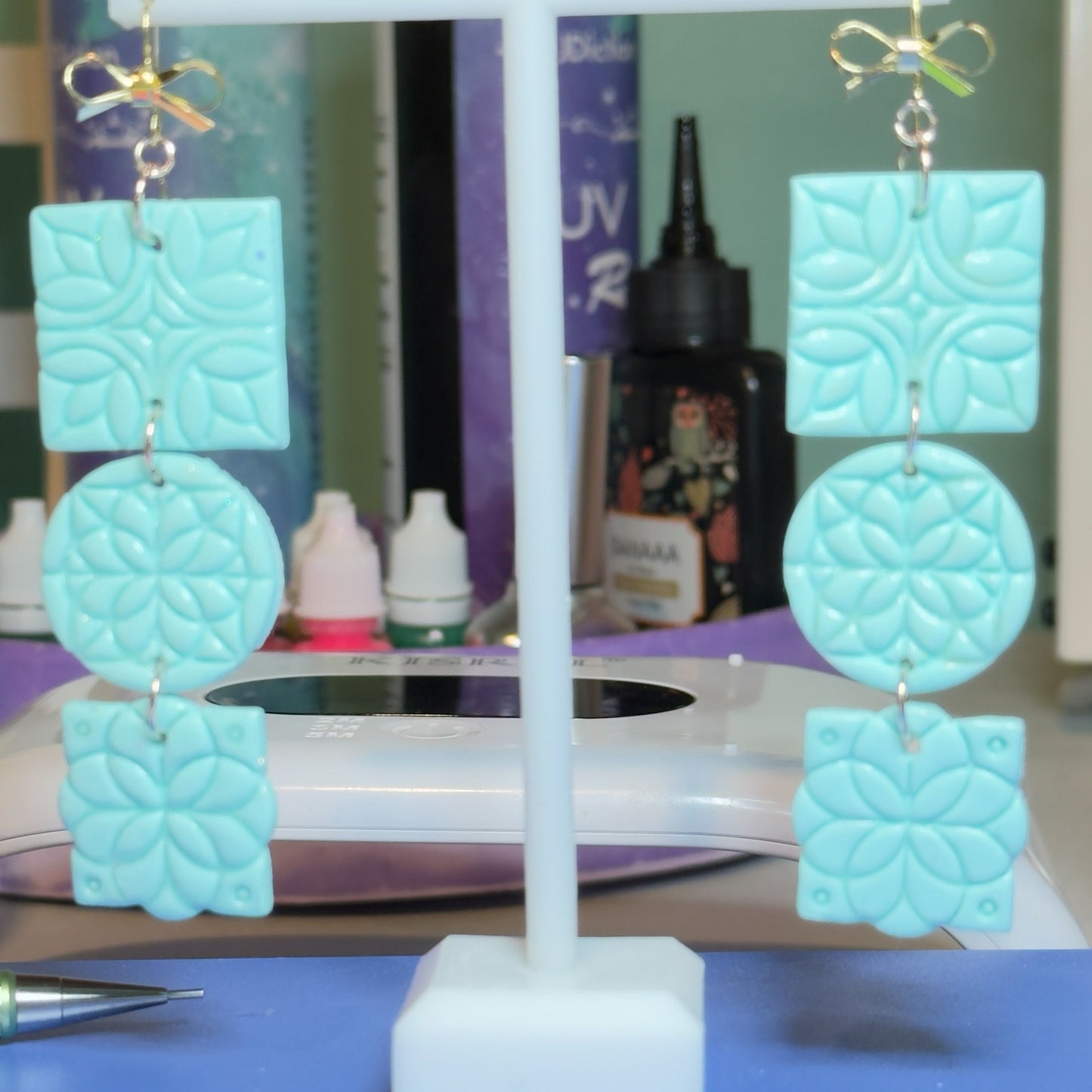 Blue Bottle Crafts light blue polymer clay drop earrings featuring geometric floral patterns and gold-tone bows.
